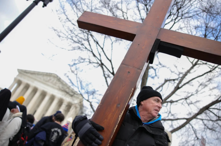 A man holds a cross outside of the Supreme Court, credit Bryan Dozier, Middle East Images, AFP